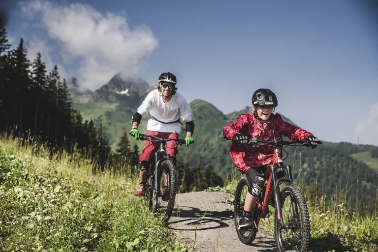 Ein Vater mit seinem Kind beim Mountainbiken auf dem Maiskogel Trail in Kaprun – actionreiche Bike-Erlebnisse für die ganze Familie inmitten der grünen Alpenlandschaft des Salzburger Landes.
