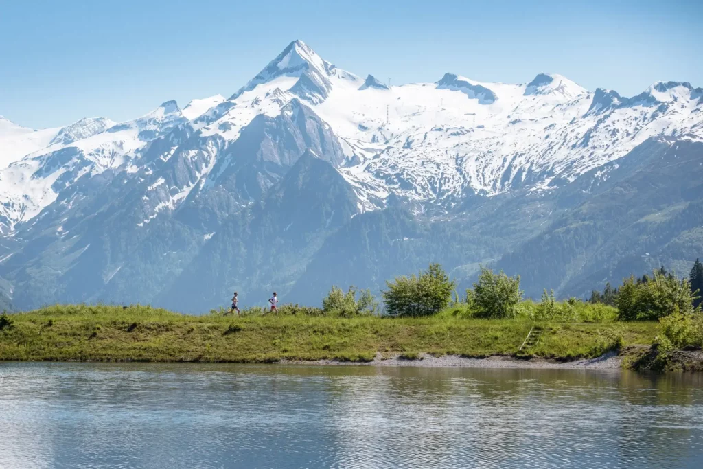Zwei Wander:innen am Speichersee mit Blick auf das schneebedeckte Kitzsteinhorn in Kaprun – Sommerurlaub in der Region Zell am See-Kaprun mit Wandern, Bergpanorama und Alpenidylle im Salzburger Land.