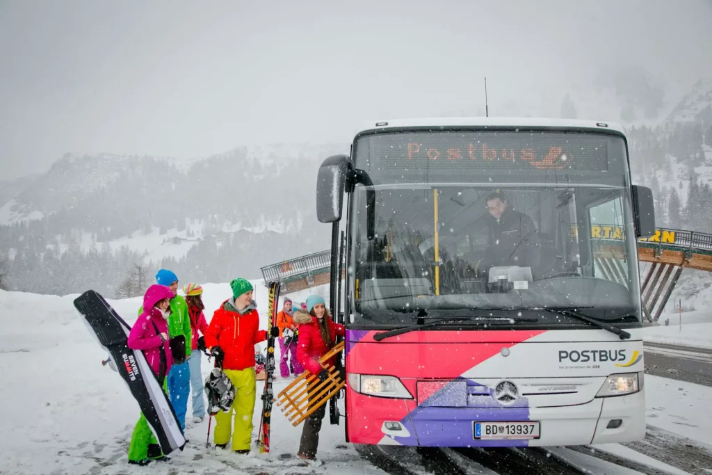 Skifahrer:innen steigen bei Schneefall in einen ÖBB Postbus im Salzburger Land - Kostenloser Skibus in der Region Kaprun - Zell am See.