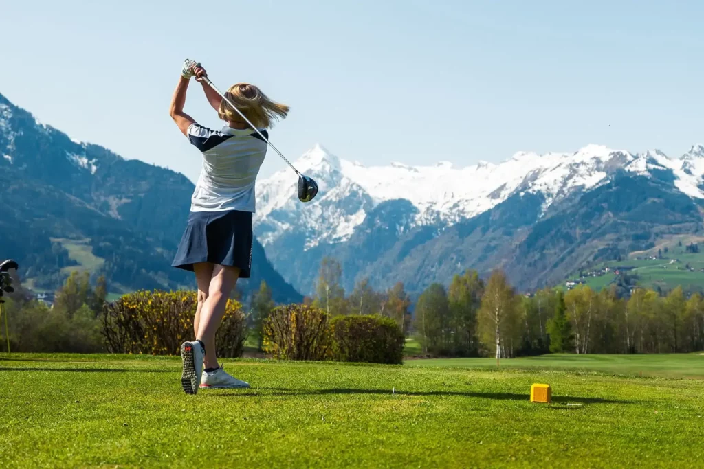 Golferin beim Abschlag am Golfplatz Zell am See-Kaprun in Kaprun mit Blick auf das Kitzsteinhorn, die Alpen und die Berglandschaft im Salzburger Land.